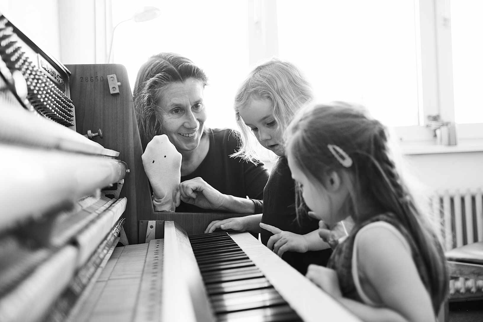 Kinder lernen das Klavier spielerisch kennen. Klavierlehrerin mit Sockenpuppe und Mädchen am Klavier.