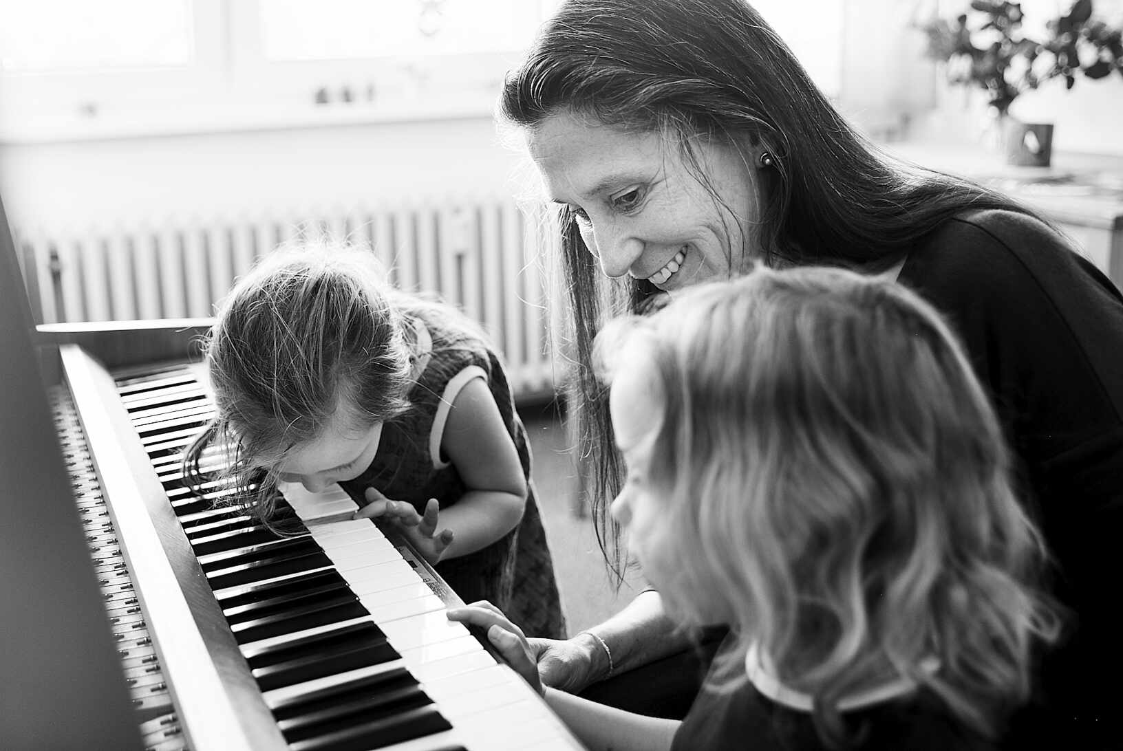 Mädchen erkunden die Klaviertasten und werden von Klavierlehrerin ermuntert.